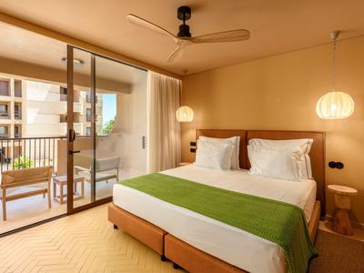 Modernes Hotelzimmer mit Doppelbett, grünem Überwurf und Balkon mit Stühlen.