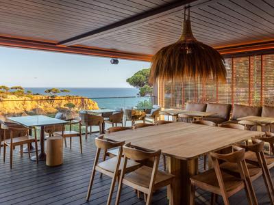 Espace de restaurant ouvert en bord de mer avec tables en bois, chaises et vue sur les falaises.