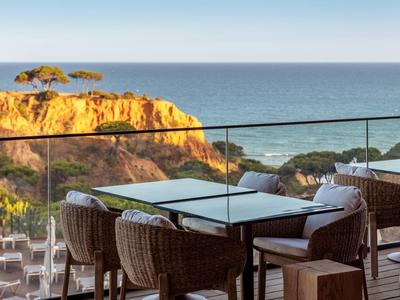 Terrasse avec tables et chaises donnant sur la mer et les falaises sous un ciel bleu.