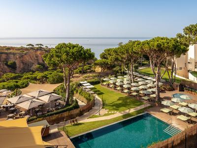Ein Hotelpool mit Sonnenschirmen, umgeben von Bäumen mit Blick auf das Meer.