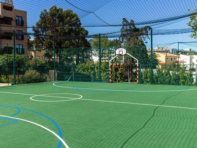 Leerer Outdoor-Sportplatz mit grünem Kunstrasen und Basketballkorb in Hotelanlage.