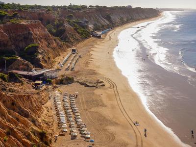 Plage de sable avec parasols à côté de falaises rouges et océan au coucher du soleil
