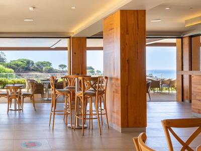 Restaurant d'hôtel lumineux avec mobilier en bois et vue sur la mer à travers de grandes fenêtres.