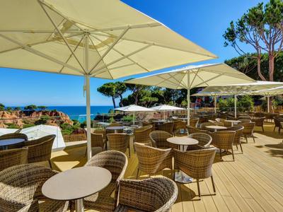 Terrasse avec chaises en osier et tables sous des parasols avec vue sur la mer par temps clair.
