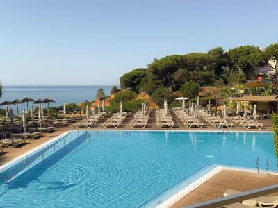 Piscine de loisirs avec transats et vue sur la mer dans une station hôtelière.