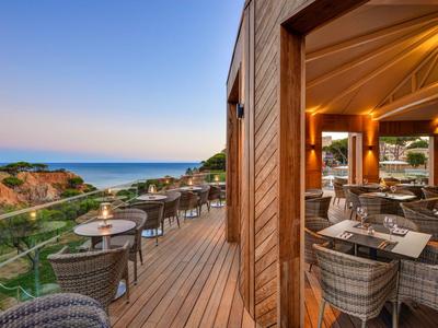Terrasse mit Tischen und Stühlen mit Blick auf die Küste bei Sonnenuntergang.