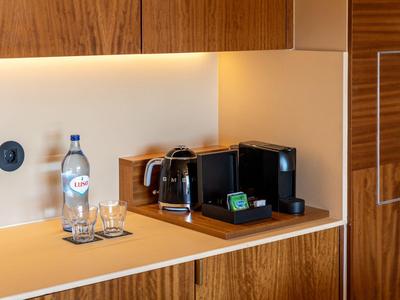 Küchenbereich mit Kaffeemaschine, Wasserflasche und Gläsern auf einer Holzarbeitsplatte.