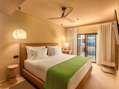 Modernes Hotelzimmer mit Doppelbett, grünem Überwurf und Balkon mit Ausblick.