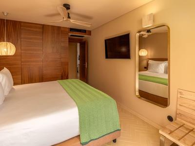 Gemütliches Hotelzimmer mit großem Bett, grünem Überwurf und Wandspiegel.
