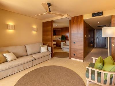 Helles Hotelzimmer mit Sofa, runden Teppich und Holzdetails.