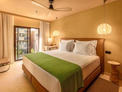 Modernes Hotelzimmer mit großem Bett, grünem Überwurf, hölzernem Nachttisch und Balkon.