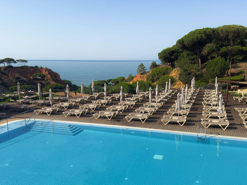 Grande piscine avec de nombreux transats et vue sur la mer sous un ciel dégagé.