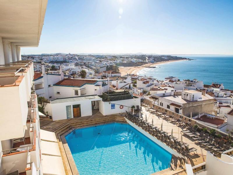 Widok na basen na tarasie hotelowym z widokiem na morze i miasto w tle.