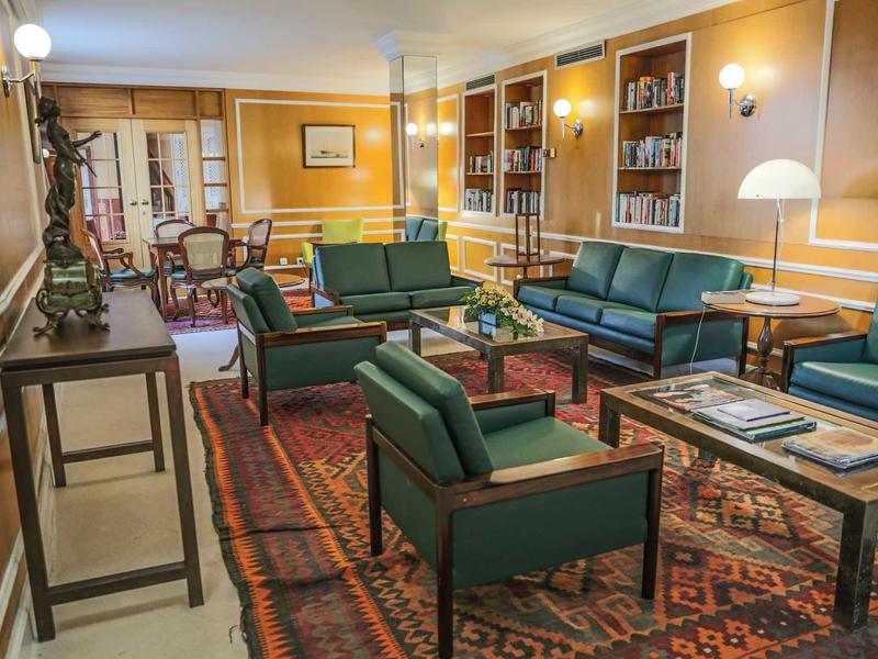 Elegancki salon z zielonymi fotelami, dywanem i regałami na książki w hotelu.