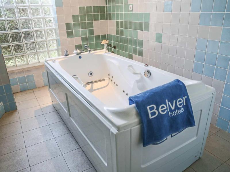 Biała wanna z hydromasażem w wyłożonym kafelkami pokoju z niebieskim ręcznikiem z hotelu Belver.