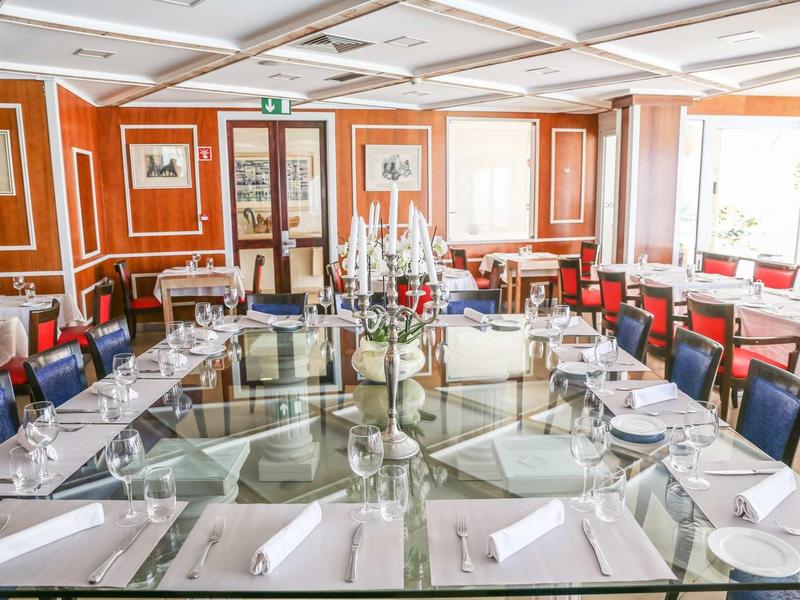 Elegancka jadalnia z okrągłym szklanym stołem, białym nakryciem i kolorowymi krzesłami w jasnym pomieszczeniu.