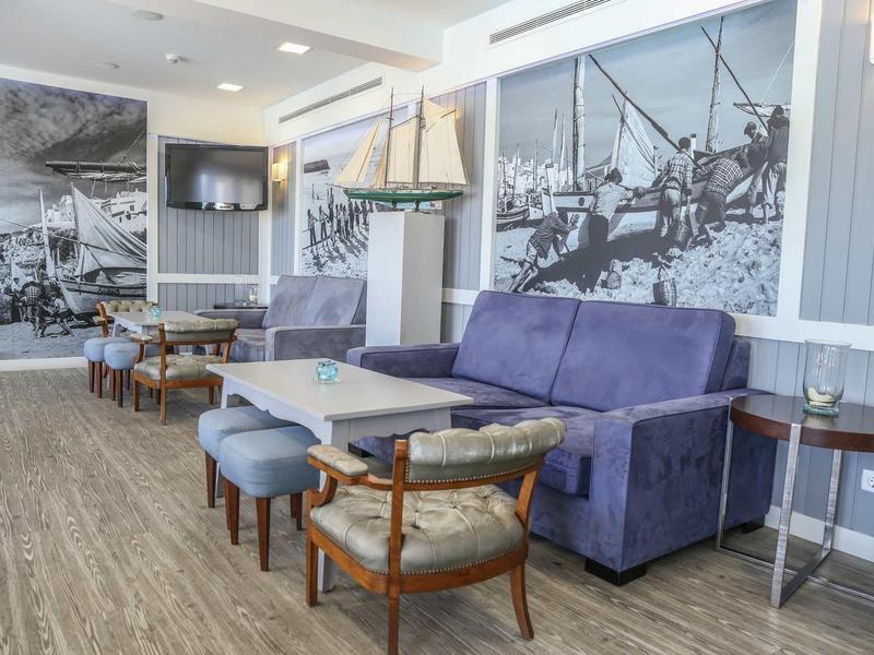 Jasny salon z niebieską kanapą, drewnianymi krzesłami i dużymi czarno-białymi zdjęciami na ścianach.