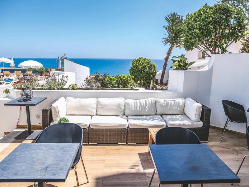 Taras z białymi ławkami, stolikami i widokiem na morze pod czystym niebem.