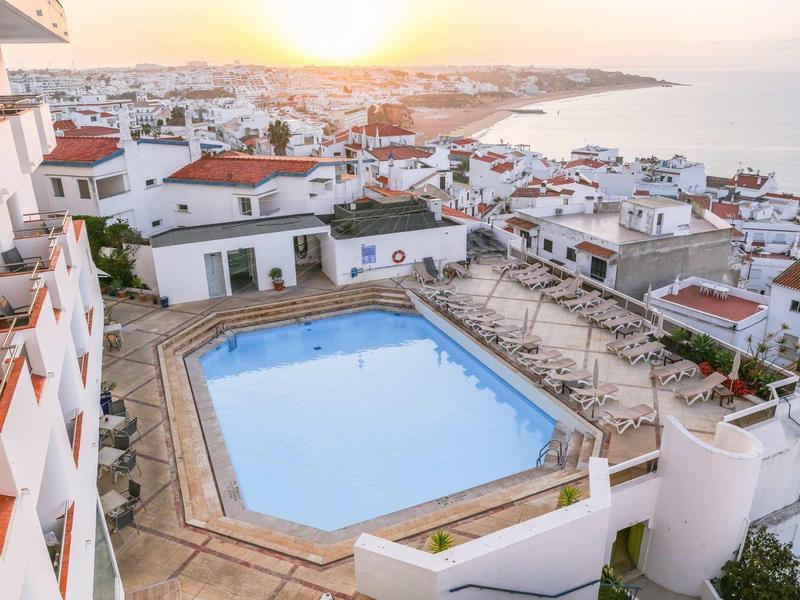 Hotel z basenem na dachu z widokiem na nadmorskie miasto o zachodzie słońca.