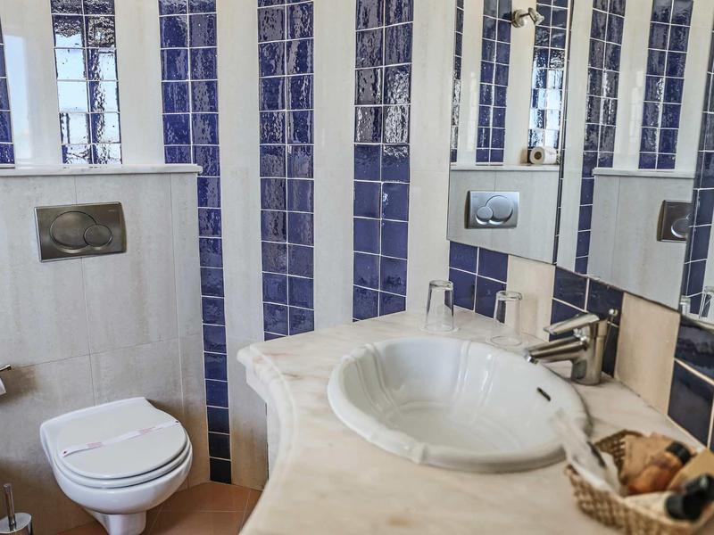 Nowoczesna łazienka hotelowa z umywalką, toaletą i niebiesko-białymi płytkami na ścianach.