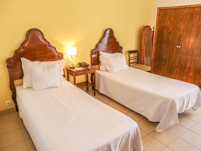 Pokój z dwoma łóżkami, drewnianymi zagłówkami, stolikiem nocnym i żółtymi ścianami.