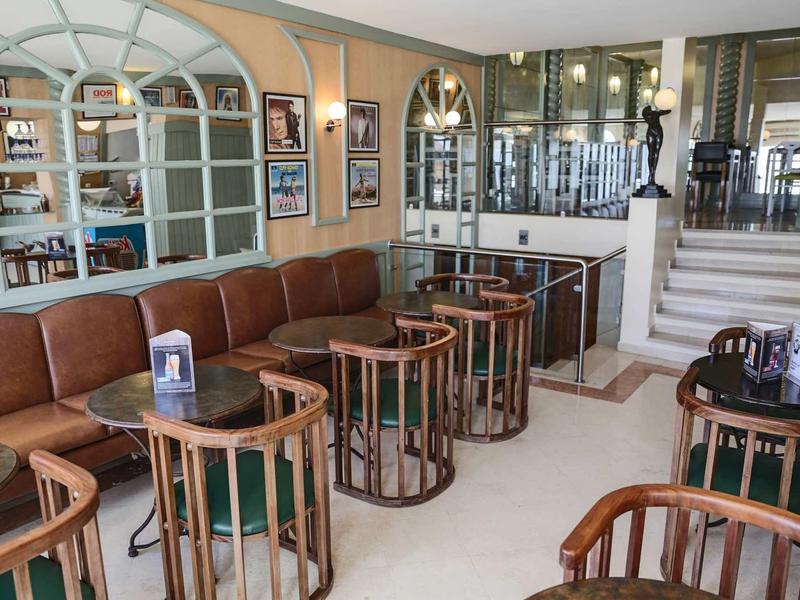 Przytulny hotelowy salon z brązowymi skórzanymi fotelami i okrągłymi drewnianymi stolikami.