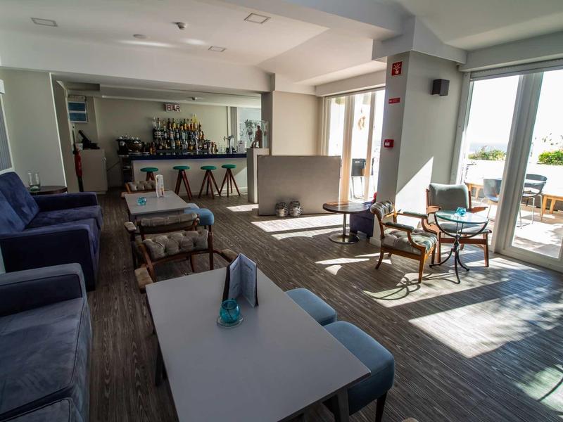 Jasny pokój hotelowy z częścią wypoczynkową, sofami i dostępem do tarasu z widokiem.