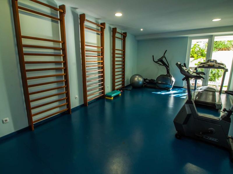 Mała siłownia z niebieską podłogą, sprzętem do ćwiczeń i drewnianymi drabinkami na ścianie.