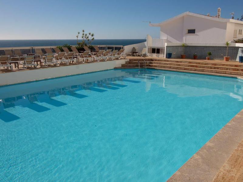 Przejrzysty basen na zewnątrz z tarasem, białymi budynkami i morzem w tle