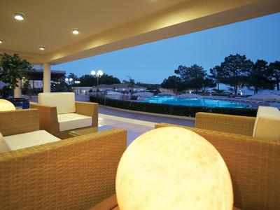 Pohodlná sedací oblast s nábytkem z proutí s výhledem na bazén za soumraku.