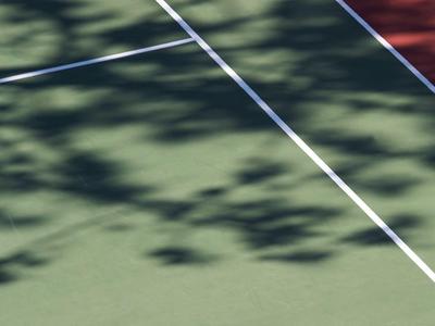 Schatten einer Person mit Tennisschläger auf Tennisplatz bei Sonnenlicht.