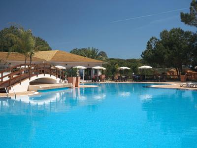 Velký bazén s visutým mostem, lehátky a slunečníky v hotelovém rezortu.