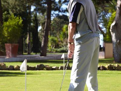Mann spielt Minigolf auf einem sonnigen, grünen Platz mit Bäumen im Hintergrund.