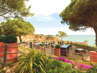 Terrasse mit Stühlen und Tischen in einem Garten mit Meeresblick unter blauem Himmel