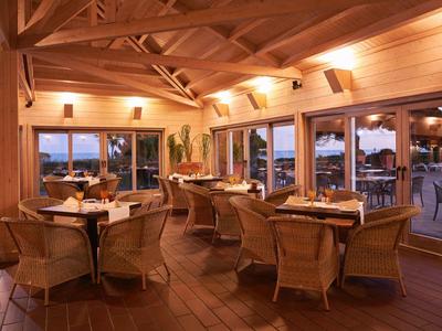 Dřevěný interiér restaurace se stoly a židlemi, velká okna s výhledem ven za soumraku