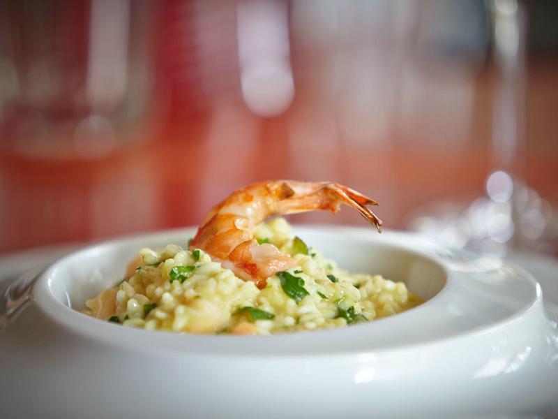 Talíř s krémovým rizotem ozdobený krevetou a bylinkami.