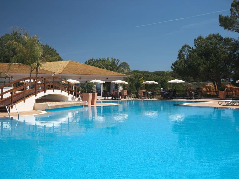 Velký bazén s visutým mostem, lehátky a slunečníky v hotelovém rezortu.