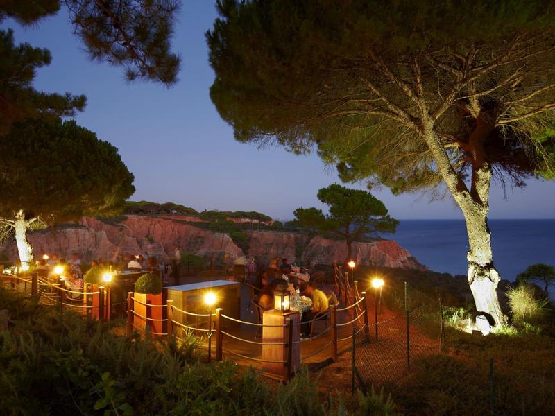 Večerní pohled na osvětlenou vyhlídkovou plošinu obklopenou zelení s výhledem na moře.