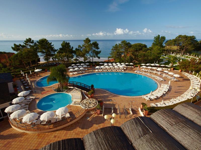 Bazén s lehátky a výhledem na moře za slunečného počasí v dovolenkovém hotelu.