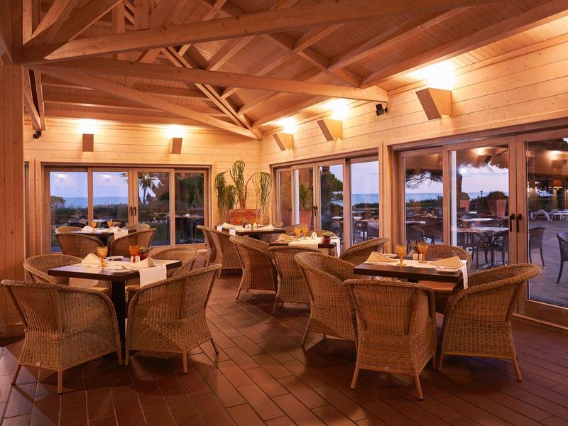 Dřevěný interiér restaurace se stoly a židlemi, velká okna s výhledem ven za soumraku