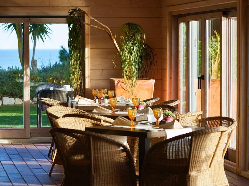 Jídelní kout s proutěnými židlemi a prostřeným stolem v dřevěném domě s výhledem na moře