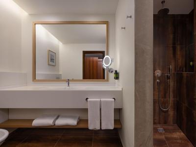 Moderne Hotel-Badezimmer mit großem Spiegel, Waschtisch und begehbarer Dusche.
