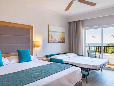 Moderne hotelkamer met groot bed, uitschuifbed, balkon met zeezicht en plafondventilator.