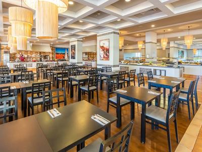 Ruim restaurantinterieur met meerdere tafels en stoelen, heldere verlichting en houten vloer.