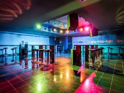 Lege nachtclub met kleurrijke lichten die op tegelvloer en bar reflecteren.