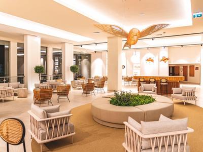 Ruime hotellobby met moderne meubels en gezellige zithoeken onder warme verlichting.