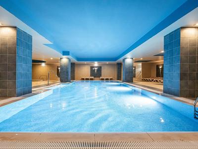 Overdekt zwembad met blauwe plafond, zuilen en zitgedeelte in een hotel spa.