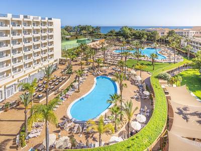 Resort met zwembaden, ligstoelen, palmbomen en zee op de achtergrond onder een heldere lucht.