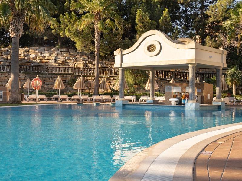 Resortzwembad met bar in het water, omgeven door ligstoelen en palmbomen.