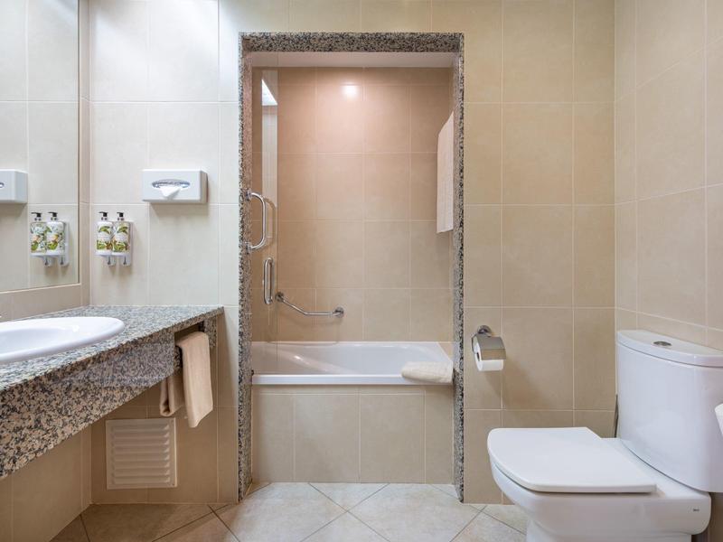 Moderne hotelbadkamer met bad, toilet, wastafel, granieten aanrecht en beige muren.